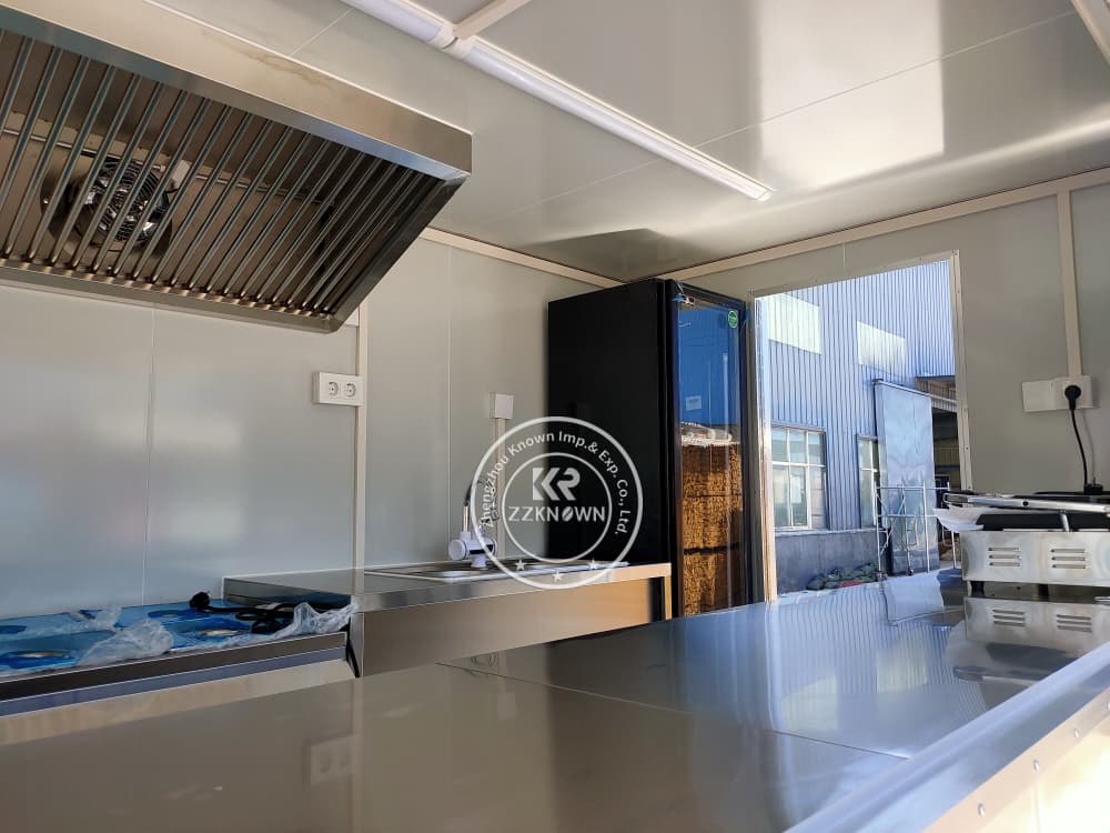 Stainless steel kitchen setup with dual sink, storage cabinets, and mounted cash box
